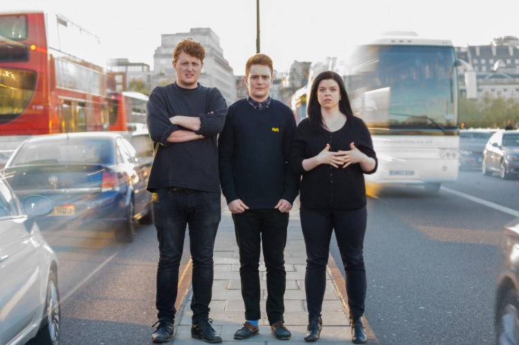 Comedy trio Minor Delays promo shoot standing between busy traffic on Waterloo Bridge